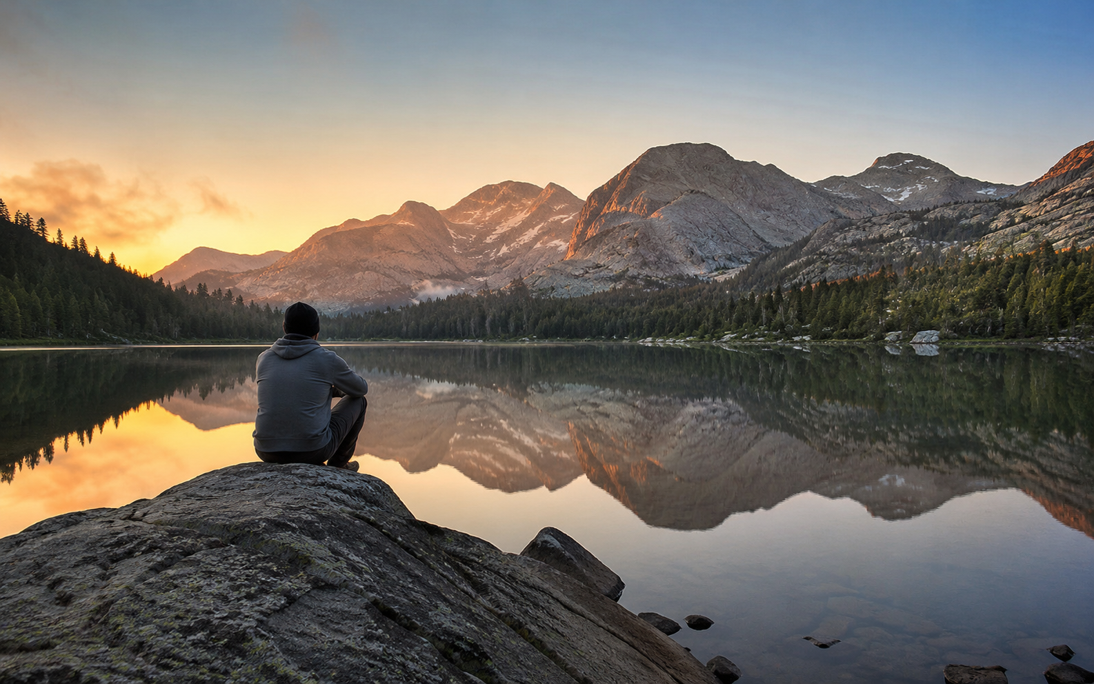 A person sitting by a mountain lake at sunrise